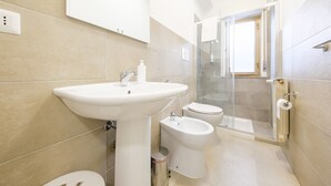 A bathroom with a sink, bidet, toilet, and a glass shower enclosure.