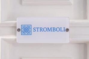 Una puerta blanca con un letrero que dice 'STROMBOLI' y un emblema azul decorativo.