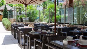 An outdoor dining area with wicker tables and chairs, large umbrellas, and a view of greenery and buildings. - Honeymoon Suite in Cannes (Cannes)