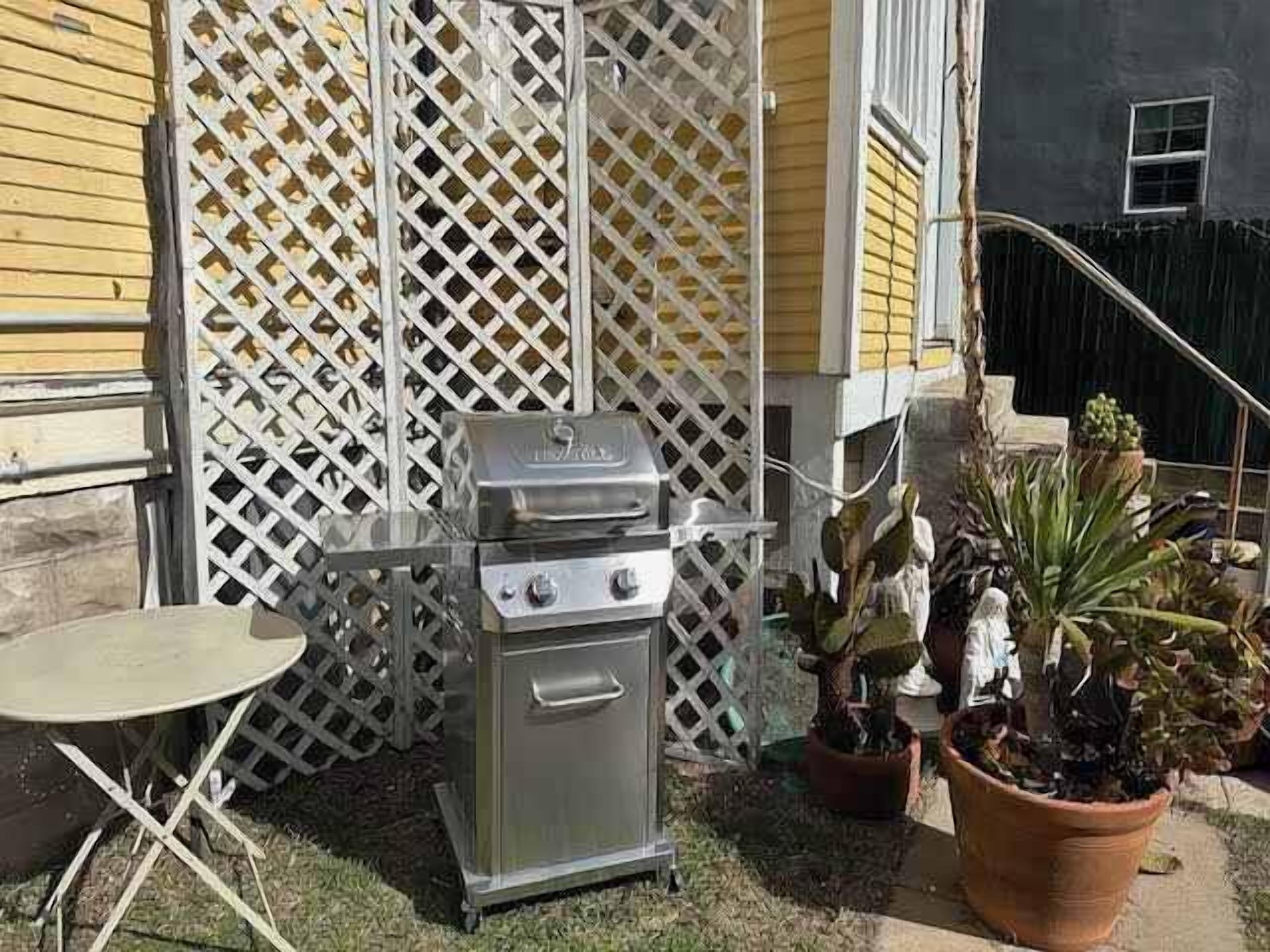 Un patio exterior con una parrilla de acero inoxidable, una mesa plegable y plantas en macetas.