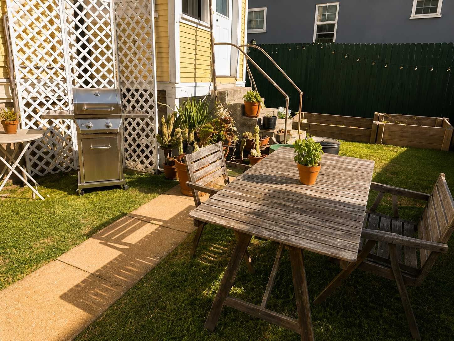 A patio with a wooden table and chairs, surrounded by potted plants and a grill.