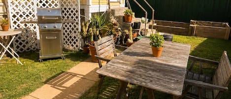 A patio with a wooden table and chairs, surrounded by potted plants and a grill.