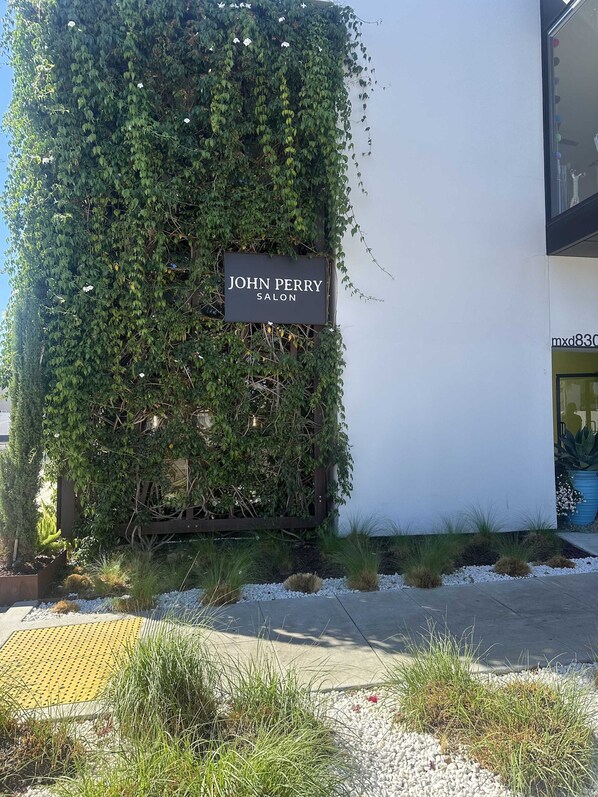 A building with a sign reading "JOHN PERRY SALON" partially covered by ivy.