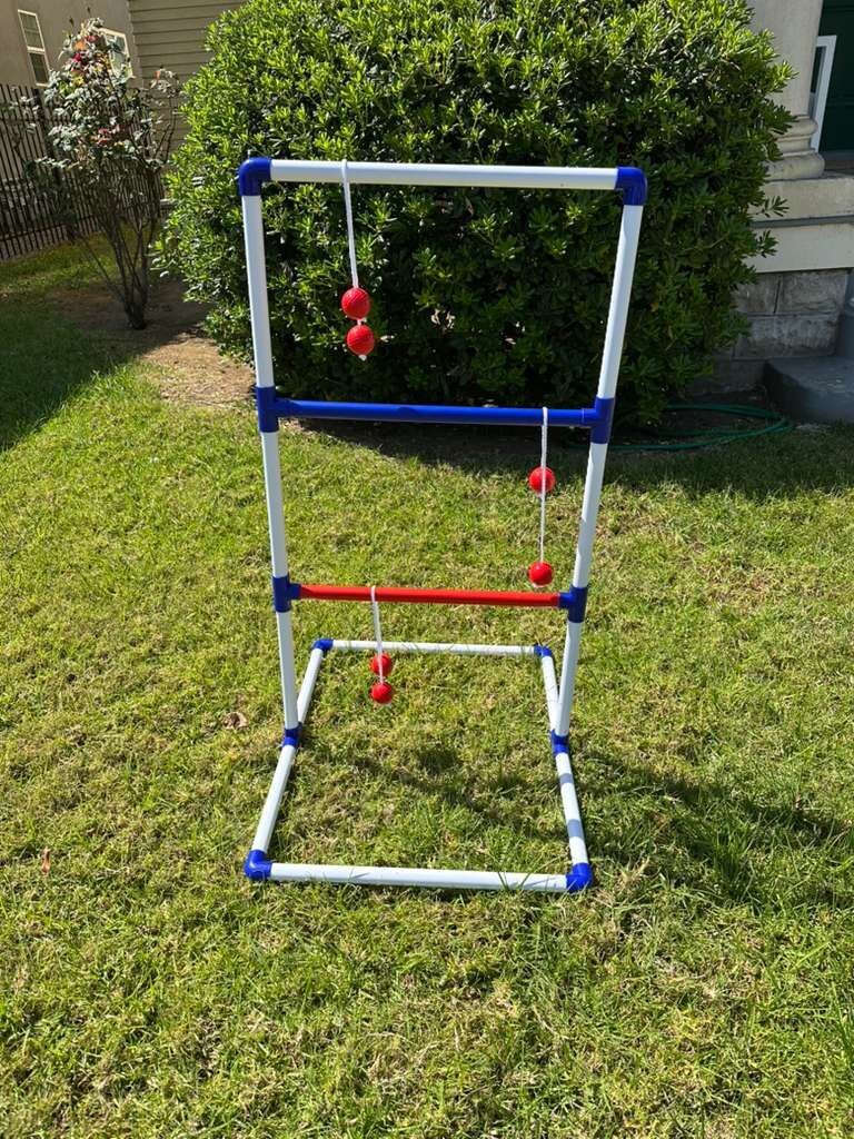 A metal frame structure with red spherical objects hanging from it, set on a grassy lawn.