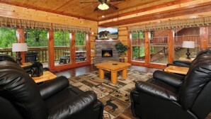 Interior acogedor de una cabaña con chimenea, asientos de cuero y ventanas amplias que ofrecen vistas al exterior.