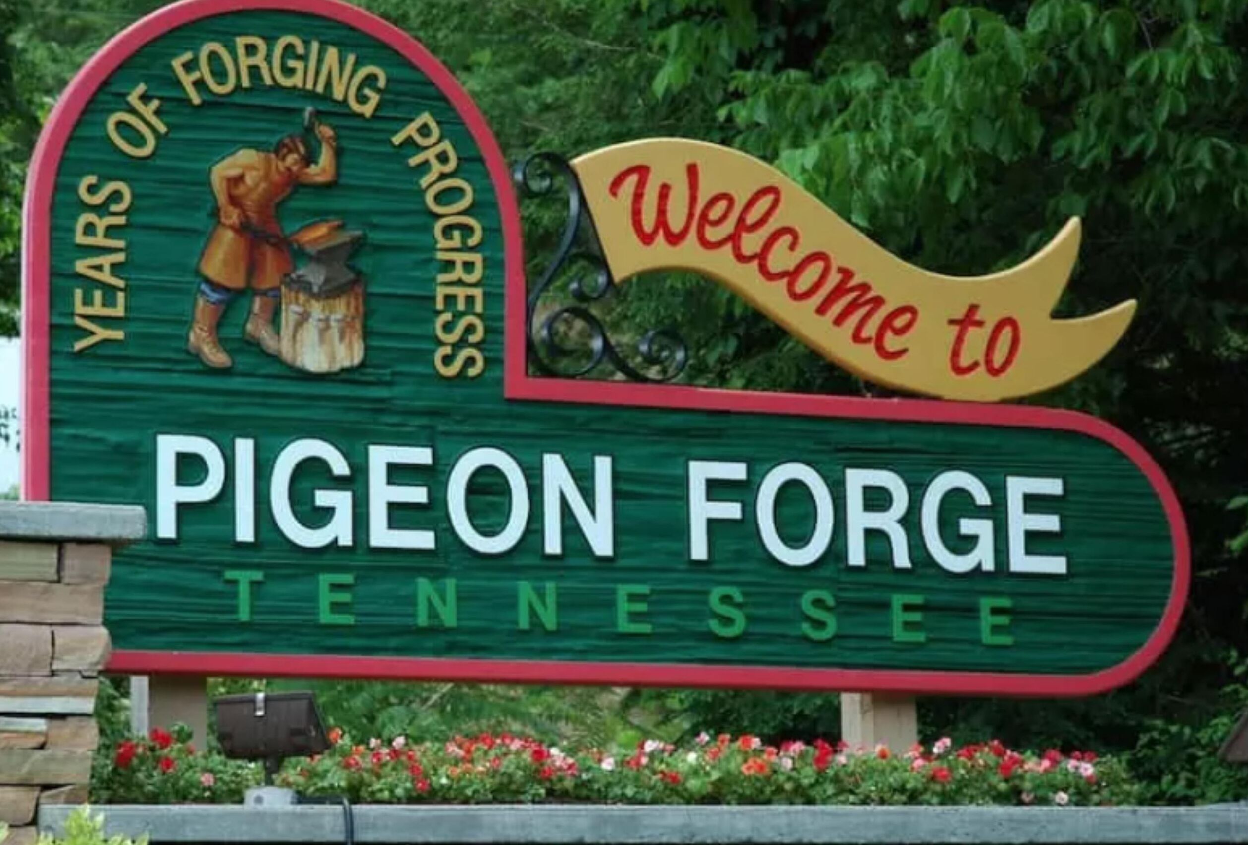 Un panneau d’accueil à l’entrée de Pigeon Forge, dans le Tennessee, avec un panneau noir et vert bordé de rouge, une boîte aux lettres noire et des fleurs rouges.
