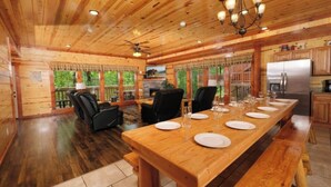 Interior de una cabaña de madera con una mesa de comedor preparada para seis personas, una chimenea y una zona de cocina.