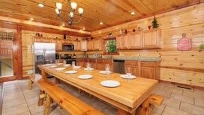 Una cocina de madera con una larga mesa de comedor preparada para seis personas, un refrigerador, un microondas y un lavavajillas.