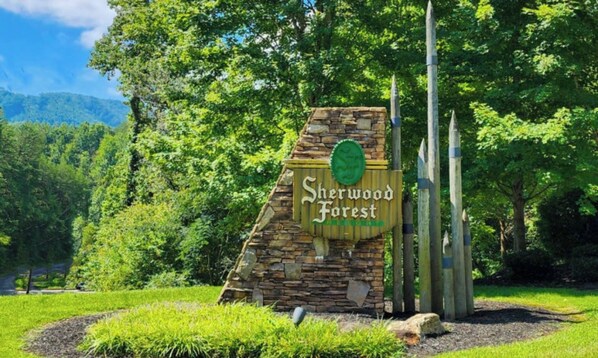 Un letrero de piedra con el texto "Sherwood Forest" rodeado de abundante vegetación y árboles.