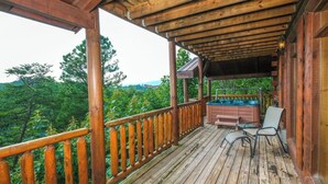 Terraza de madera con jacuzzi y sillas, con vistas a una zona boscosa.