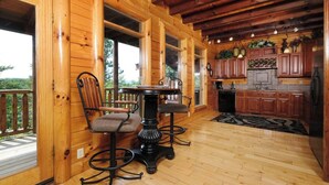 Una cabaña de madera con comedor que incluye una mesa y sillas, cocina con armarios de madera, y vistas al exterior.