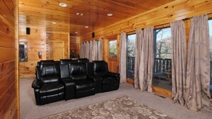 A log cabin interior with a black leather sofa, wooden walls, and large windows with curtains.