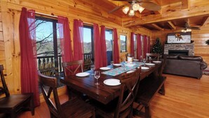 A wooden cabin interior with a dining table set for four, wooden chairs, a fireplace, and a Christmas tree.