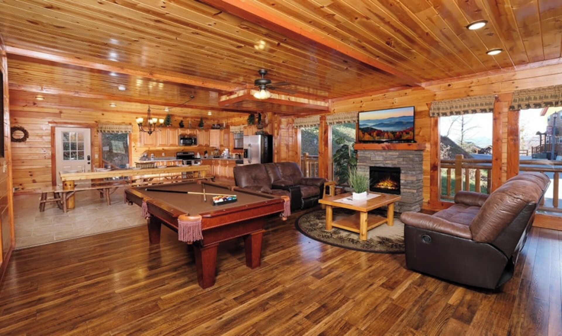 A cozy log cabin interior with a pool table, leather sofa, and a fireplace.