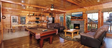 A cozy log cabin interior with a pool table, leather sofa, and a fireplace.