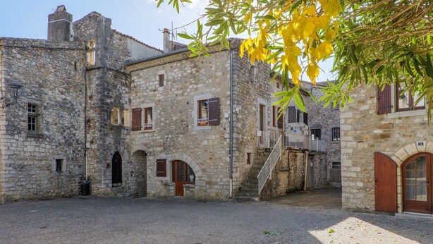 Un edificio de piedra con arcos en puertas y ventanas, un patio adoquinado y una escalera que sube a un nivel superior.