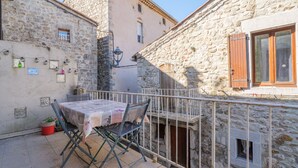 Un edificio de piedra con un balcón, una mesa con mantel y una silla.