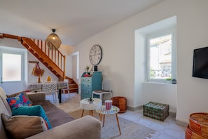 Un salon comprenant un canapé, une table basse, une horloge, un téléviseur, un escalier et une fenêtre.