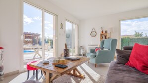 Een ruime woonkamer met een houten tafel, een bank en een stoel. Een groot raam biedt uitzicht op de omgeving.
