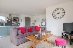 A modern living room with a grey sofa, red cushions, a wooden coffee table, a large wall clock, and a flat-screen TV. - Holiday Home 'M Vallon Pont D'arc' with Private Pool, Wi-Fi and Air Conditioning (Vallon-Pont-d'Arc)