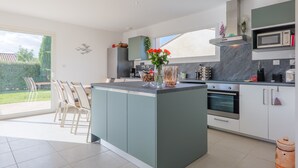 Een moderne keuken met een centraal kookeiland, ingebouwde apparatuur en een eethoek met stoelen.