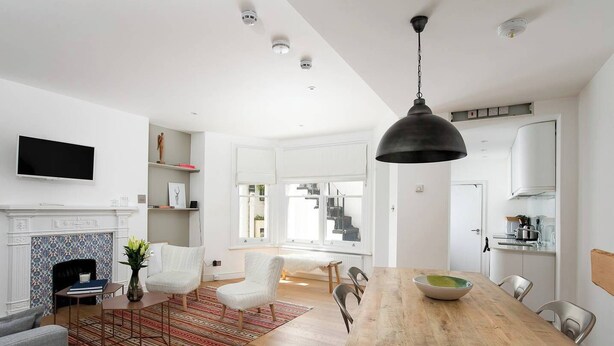 Une cuisine moderne avec une table à manger en bois, des chaises blanches et un luminaire suspendu noir.