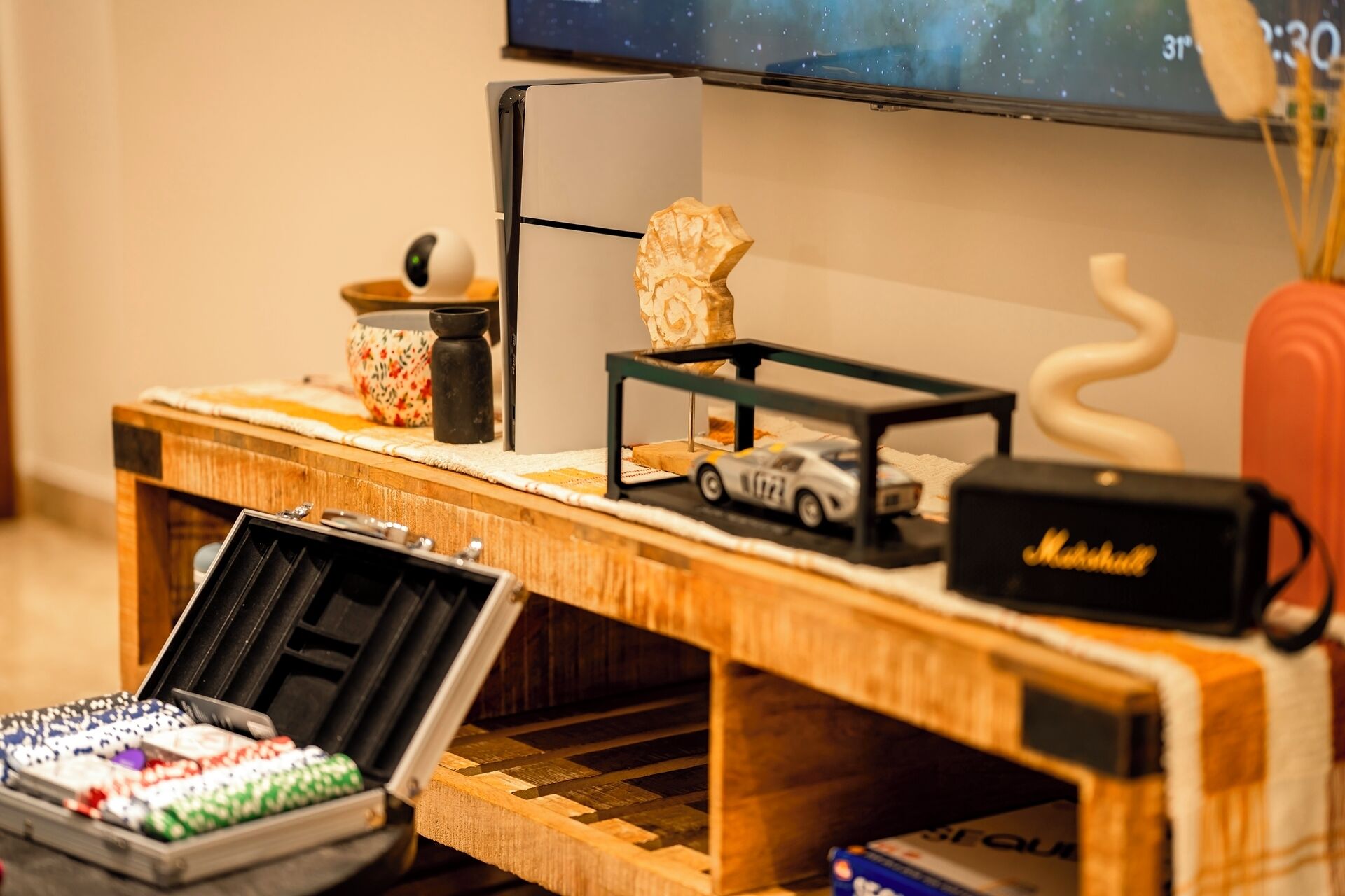 A wooden display table with a television, a small car model, a decorative rock, and a speaker.