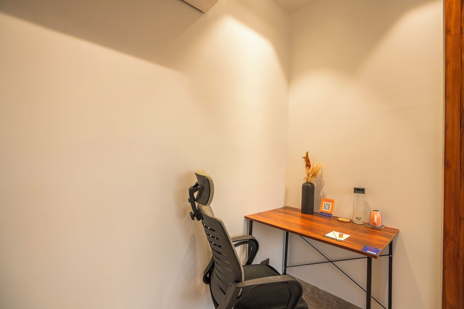 A small office space with a desk, chair, and a vase with dried flowers.