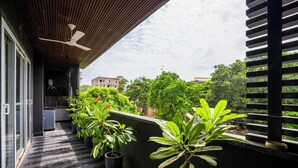 A balcony with potted plants, a ceiling fan, and a view of surrounding buildings and trees. - LiveAway Gurugram by PACK (Gurugram)