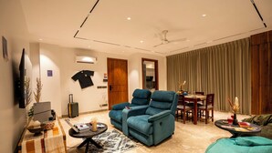 A modern living room with a sofa, a dining table with chairs, a ceiling fan, and a TV mounted on the wall. - LiveAway Gurugram by PACK (Gurugram)