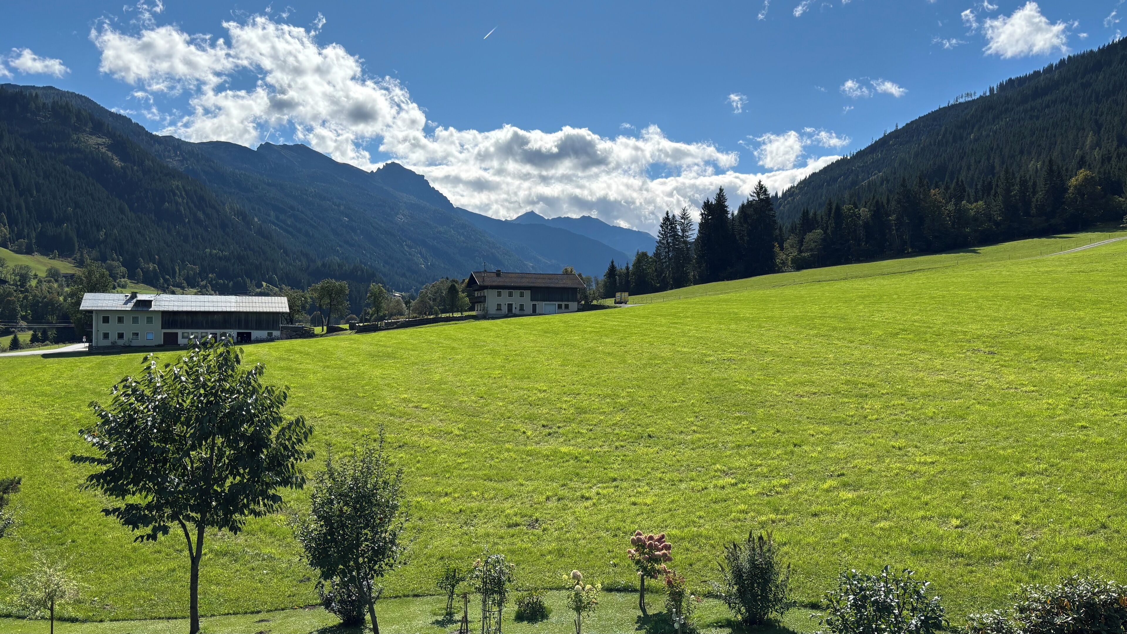 A rural landscape with a large green field, two buildings, and mountains in the background.