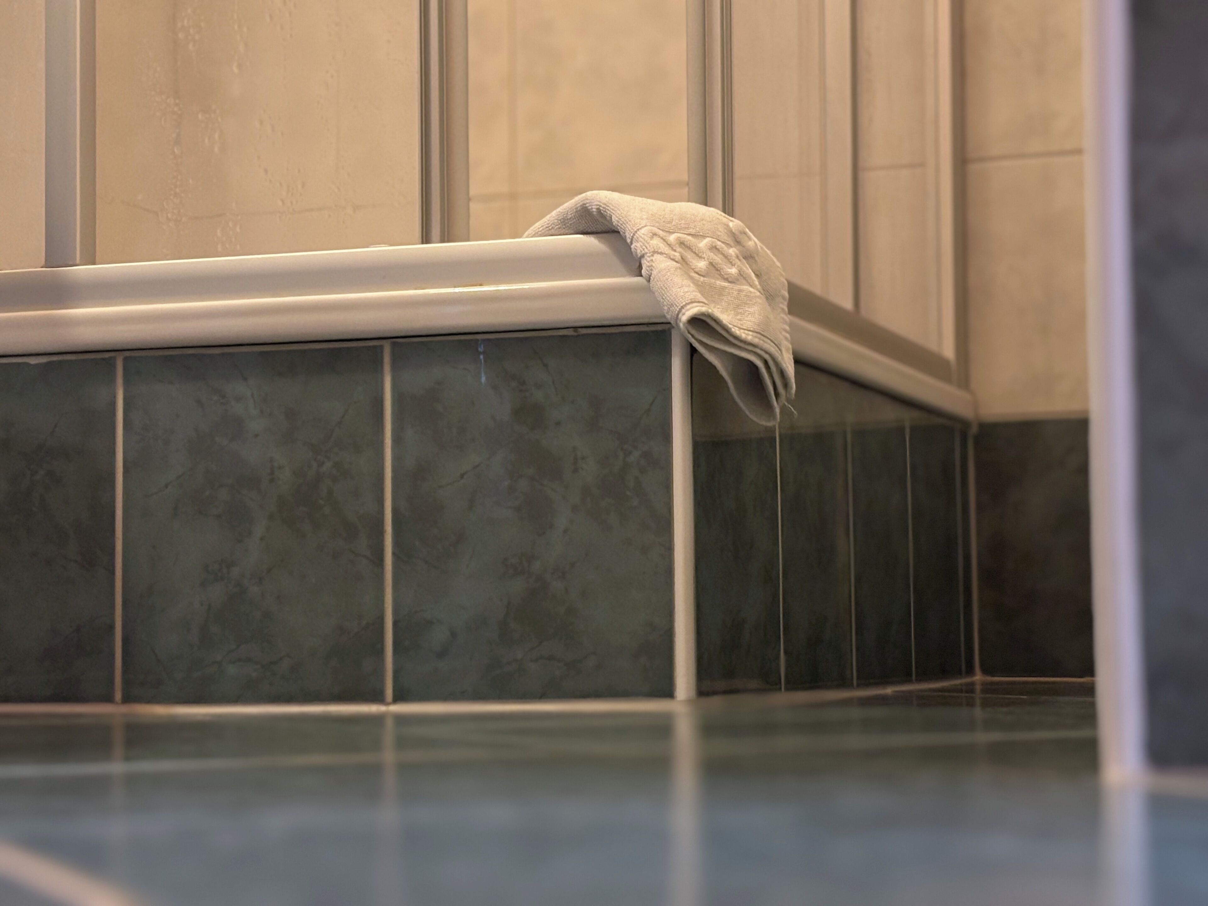 Un baño con azulejos verde oscuro y una toalla blanca sobre el borde de una bañera.