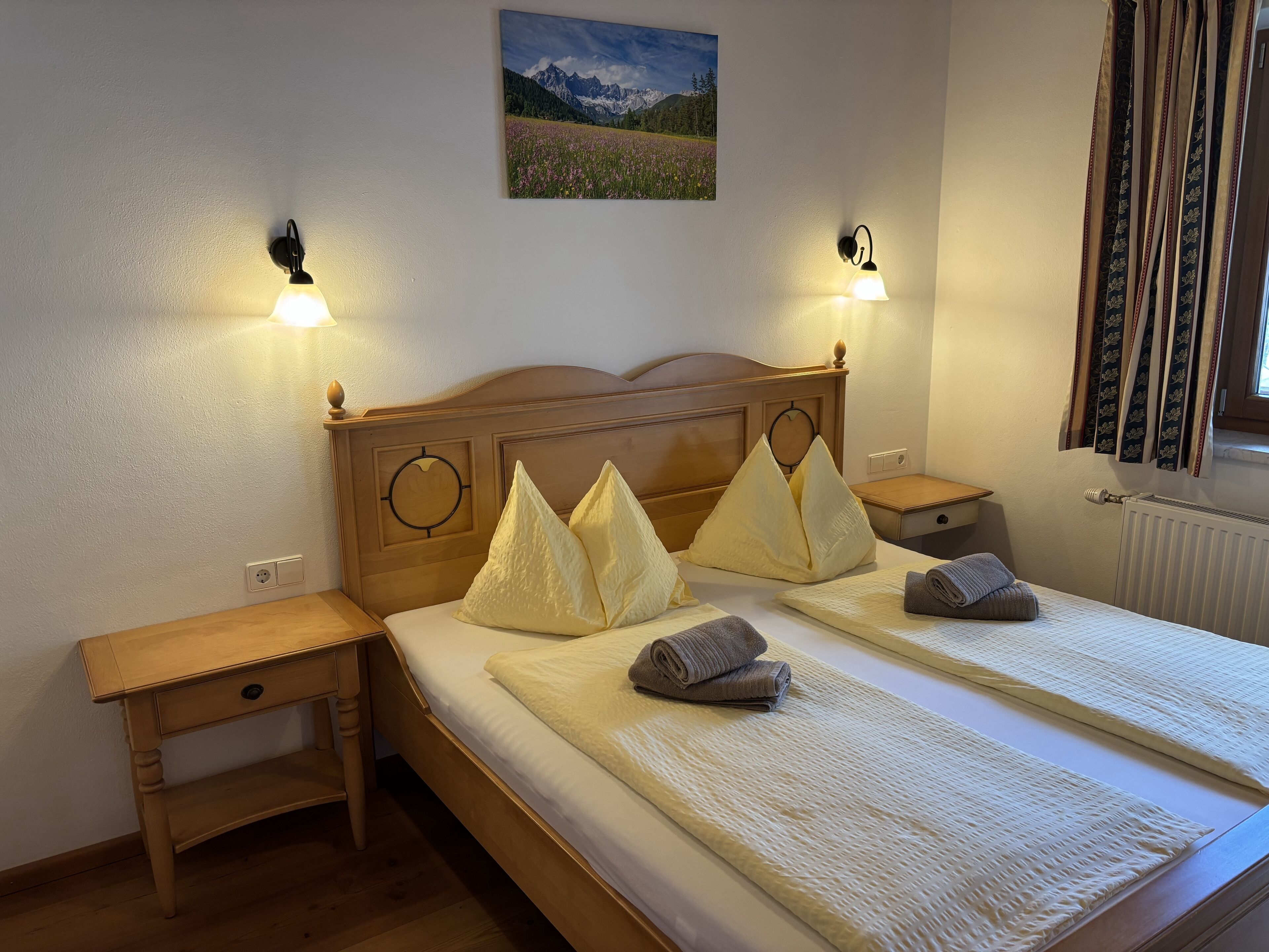 A double bed with a wooden headboard, two bedside tables, and a wall-mounted picture.