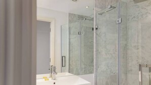 Ein modernes Badezimmer mit einer gläsernen Dusche, einem weißen Waschbecken und Marmorfliesen.