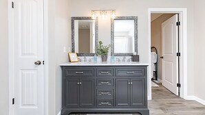 Une salle de bain avec un meuble-lavabo gris foncé, un grand miroir et un luminaire placé au-dessus du miroir.