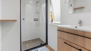 A modern bathroom with a glass-enclosed shower, a white sink, and wooden cabinets. - Apartment 'Mobile Home Le Montourey' with Balcony and Air Conditioning (Fréjus)