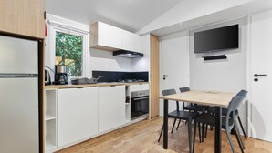 A modern kitchen with white cabinetry, a built-in oven, a coffee machine, and a dining area with a table and chairs. - Apartment 'Mobile Home Le Montourey' with Balcony and Air Conditioning (Fréjus)