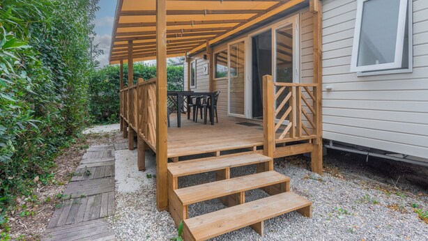 A covered wooden deck with a table and chairs, leading to a sliding glass door entrance. - Apartment 'Mobile Home Le Montourey' with Balcony and Air Conditioning (Fréjus)