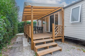 A covered wooden deck with a table and chairs, leading to a sliding glass door entrance. - Apartment 'Mobile Home Le Montourey' with Balcony and Air Conditioning (Fréjus)