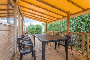 Een terras buiten met een tafel, stoelen, houten leuningen en uitzicht op groen.