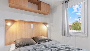 A bedroom with a bed, wooden headboard, built-in shelf, and a window with a view. - Apartment 'Mobile Home Le Montourey' with Balcony and Air Conditioning (Fréjus)