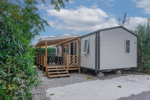 Een stacaravan met een overdekte veranda en een klein terras, omgeven door groen.
