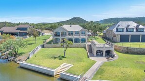 A large, multi-story house with a stone facade, a patio with outdoor furniture, and a view of a lake.