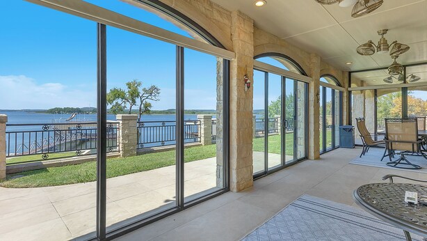 A spacious indoor area with large windows overlooking a body of water, stone pillars, and ceiling fans.