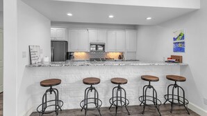A modern kitchen with white cabinetry, a granite countertop, and four bar stools.