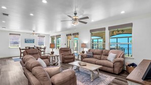 A spacious living room with a high ceiling, large windows, and a balcony with a view of the ocean.