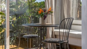 Una pequeña mesa redonda con un jarrón de flores, dos sillas y una ventana con cortinas.