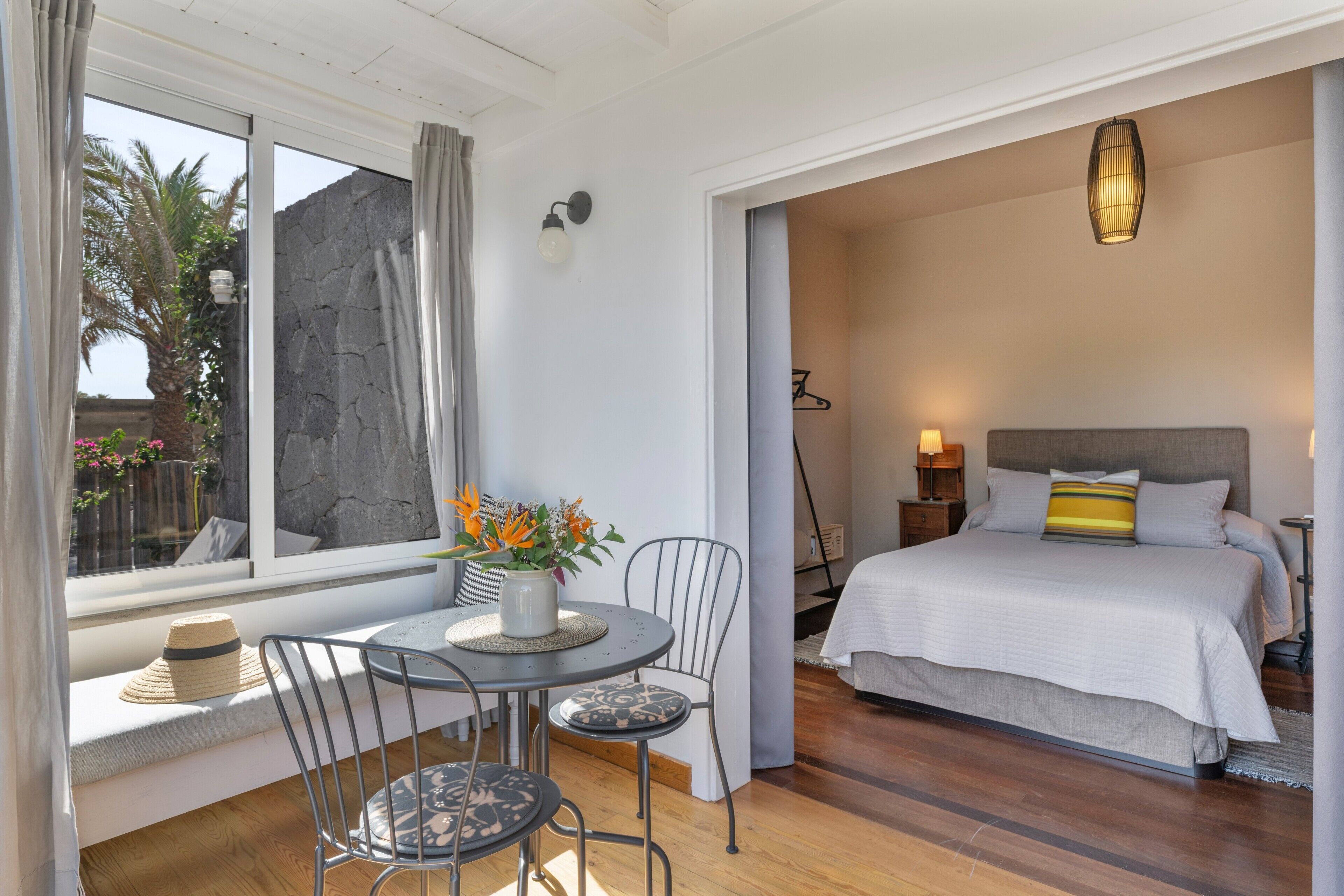 Ein Schlafzimmer mit Bett, Nachttisch, Lampe und Blick ins Freie.