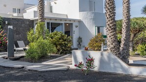 Un edificio moderno blanco con muro de piedra, palmeras y un pequeño jardín con plantas y flores.