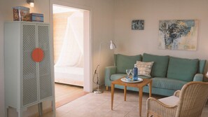 Ein Wohnzimmer mit einem grünen Sofa, einem Holztisch, einem Korbstuhl, einer Kommode mit dekorativer Front und einem Bild an der Wand.